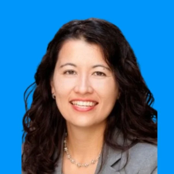 A woman with wavy dark hair smiling against a solid blue background.