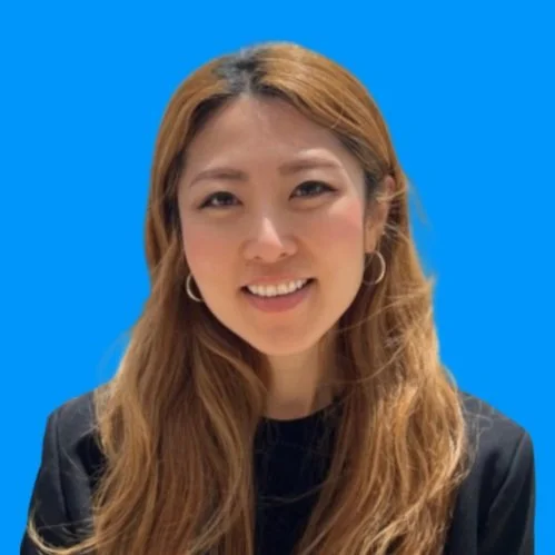 A woman with long, wavy hair, wearing a black top and hoop earrings, smiling against a blue background.