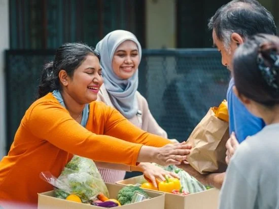 Group of smiling people sharing a meal and exchanging food outdoors.