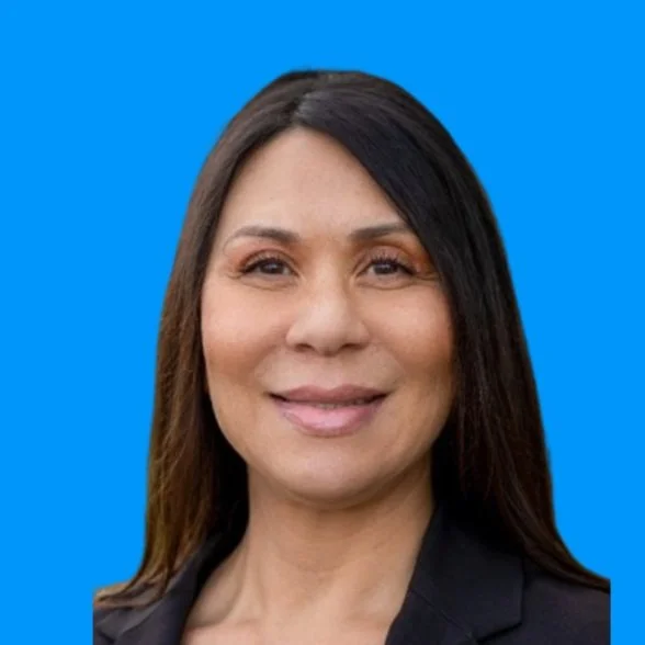 A woman with long dark hair smiling against a solid blue background.