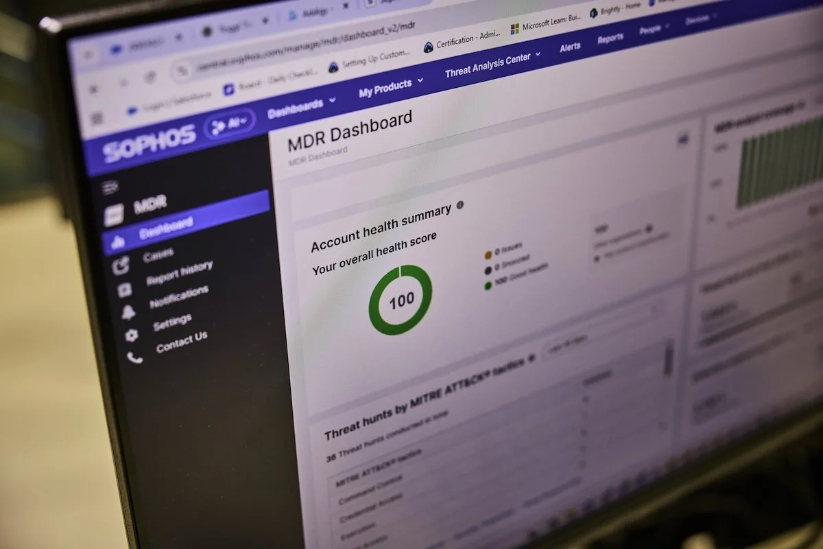 Laptop screen displaying a Sophos MDR (Managed Detection and Response) dashboard with an account health score of 100 and threat monitoring analytics visible in the interface.