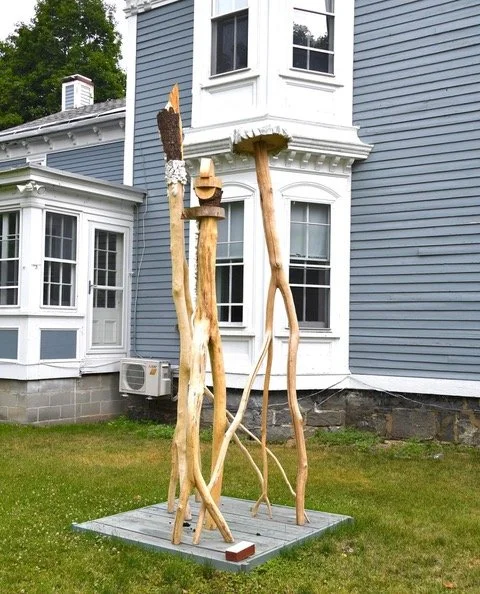 Wooden outdoor sculpture in front of gray house
