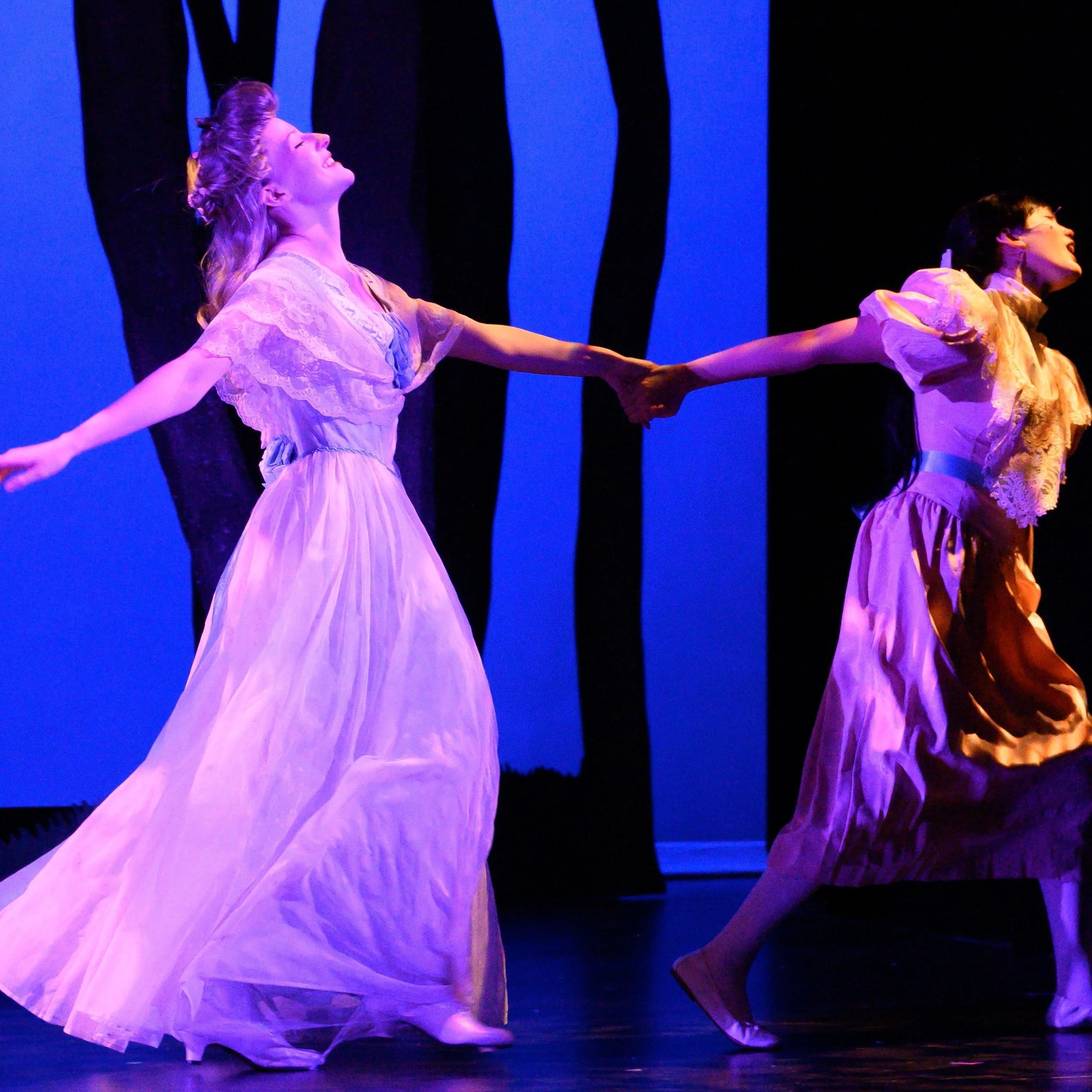 A teenager in a pink dress drags a young woman off by the hand as she flits about in a large blue ballgown.