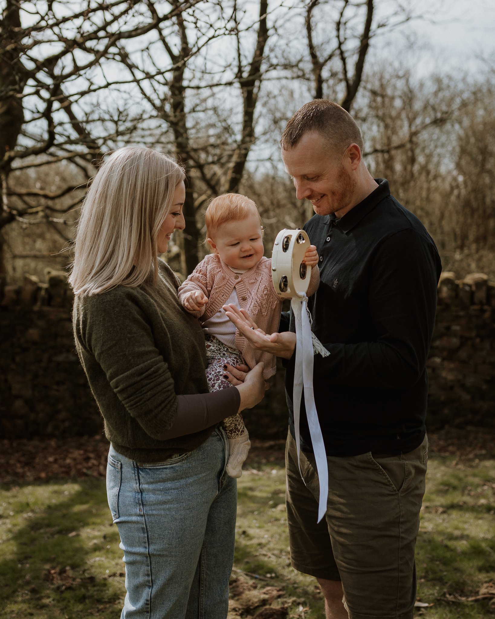Baby Orla playing with a tambourine in mum and dad's arms in Abbeystead