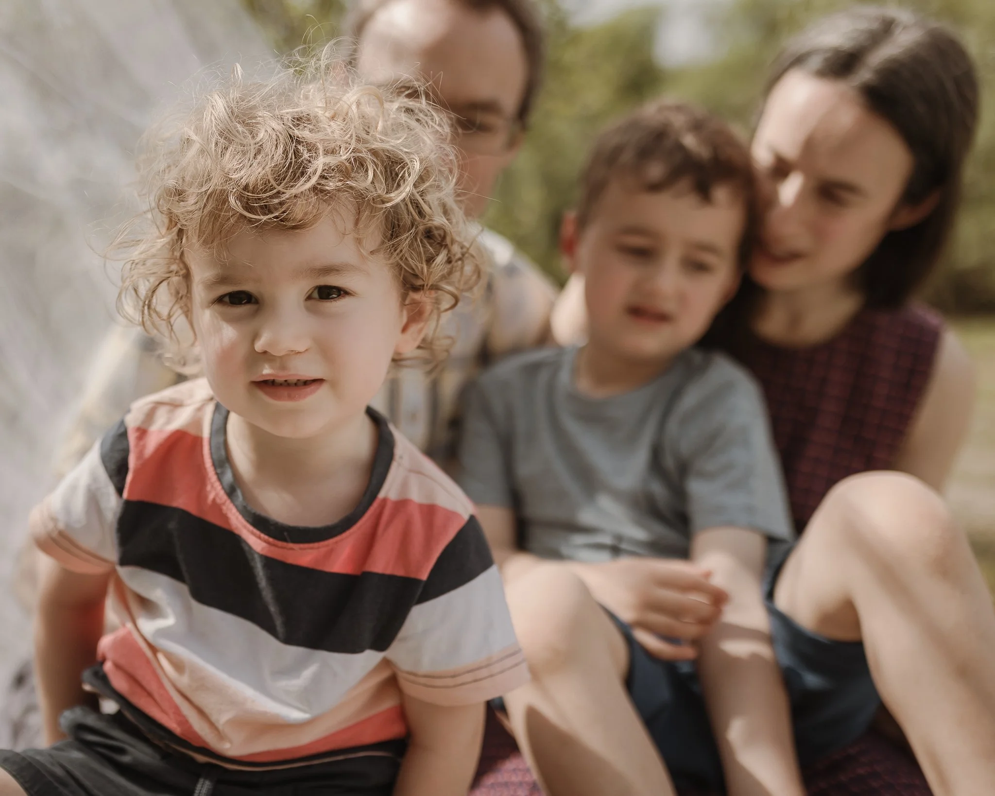 Photograph of a young boy in the foreground with his family in the background