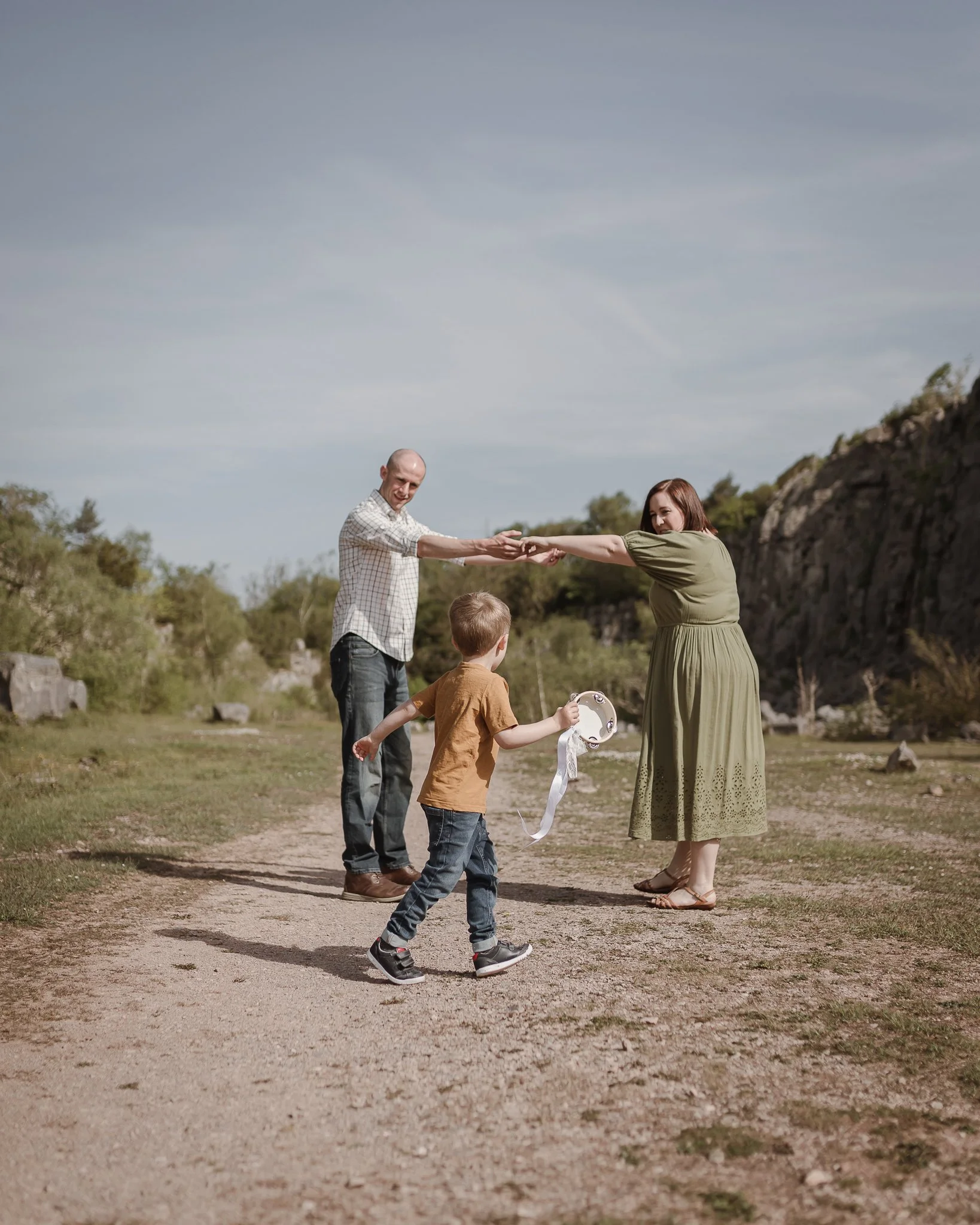 Photograph of a little boy running with a tambourine towards his mum and dader little boy who is holding a wooden plane