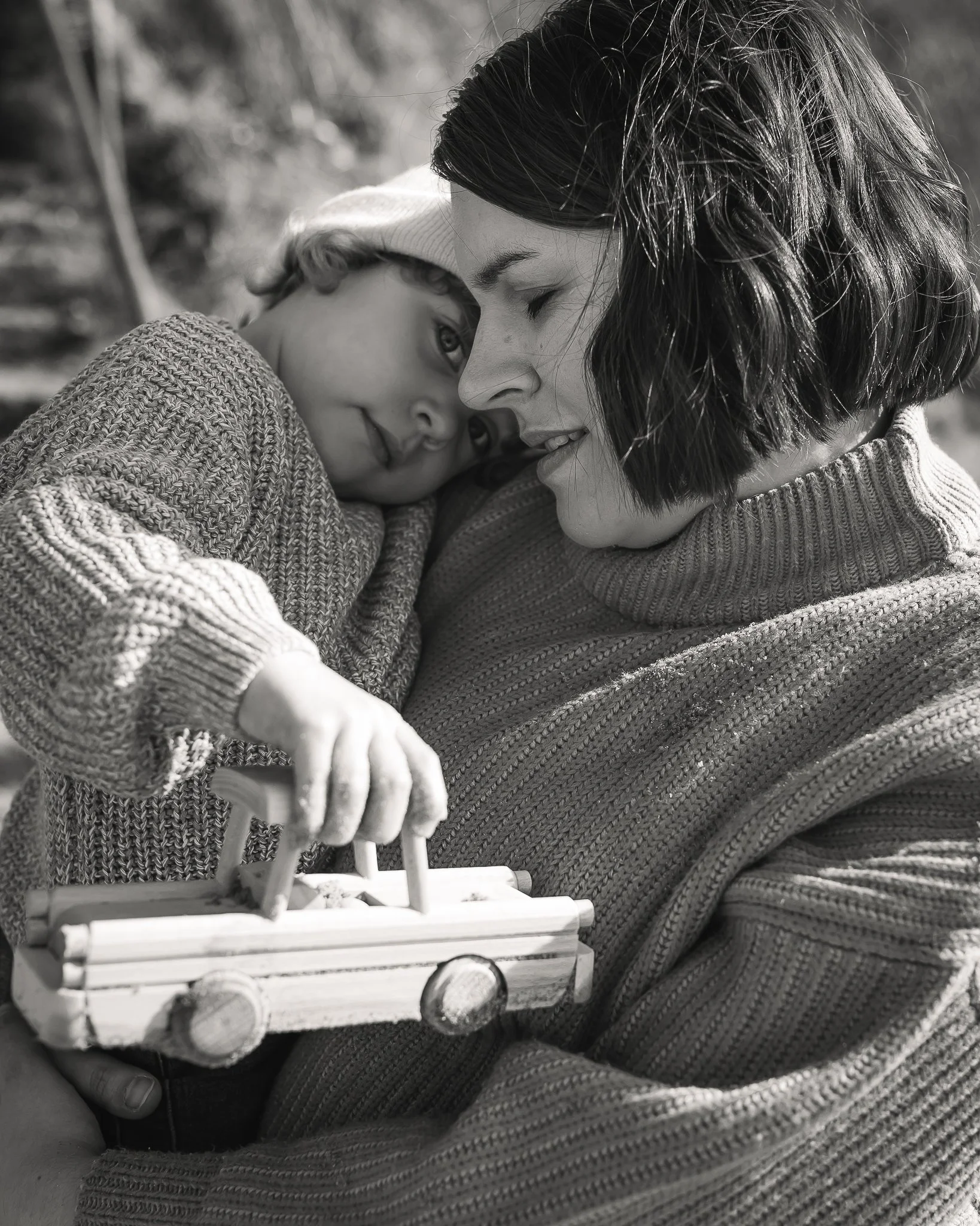 Photograph of a mother holding her daughter with a wooden car