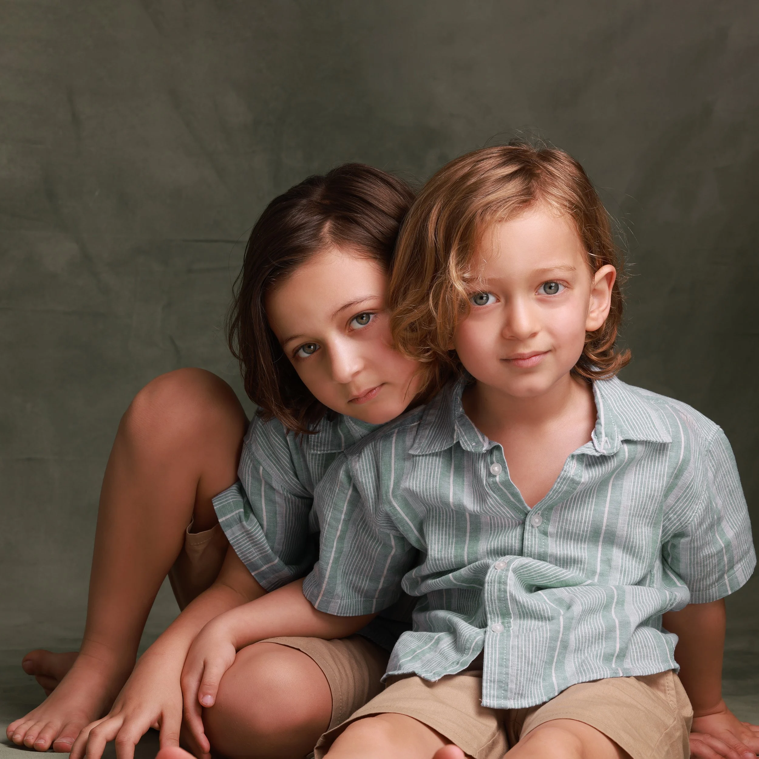 Two children, a girl with brown hair and a boy with red hair, sitting close together against a neutral background.