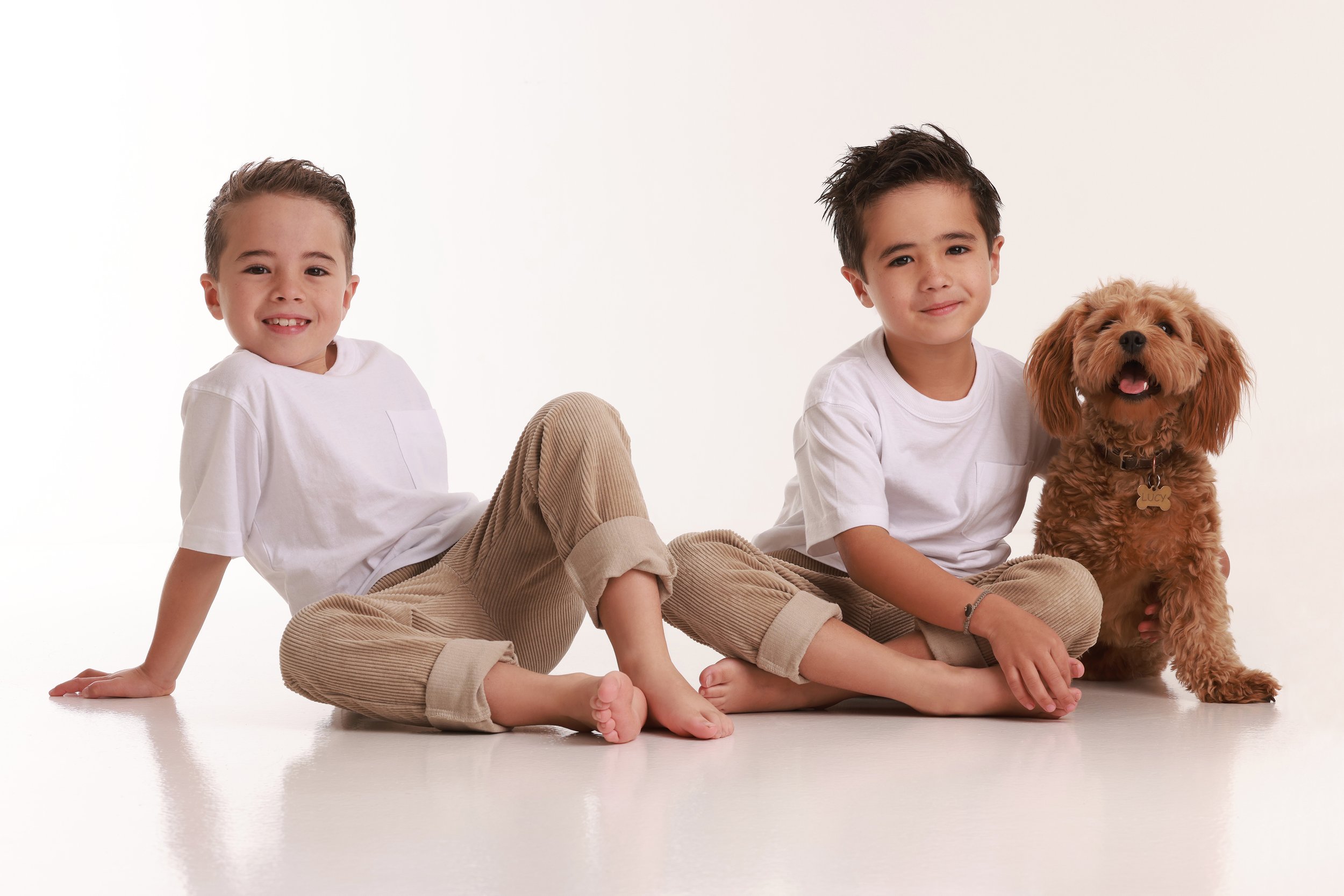 Two young boys sitting on the floor with a fluffy brown dog in a studio setting with white background.