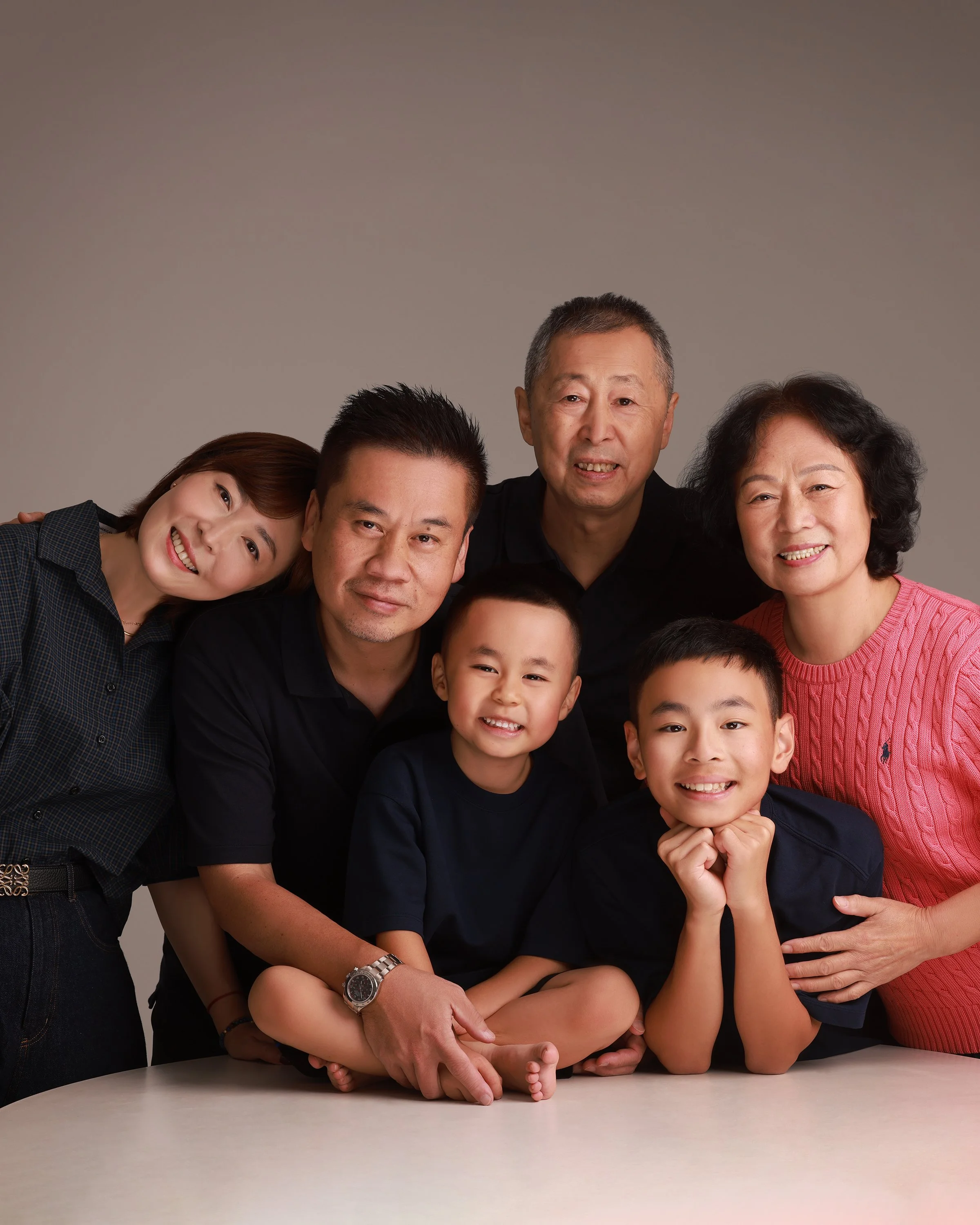 Family portrait of two adults and three children smiling together against a plain background.