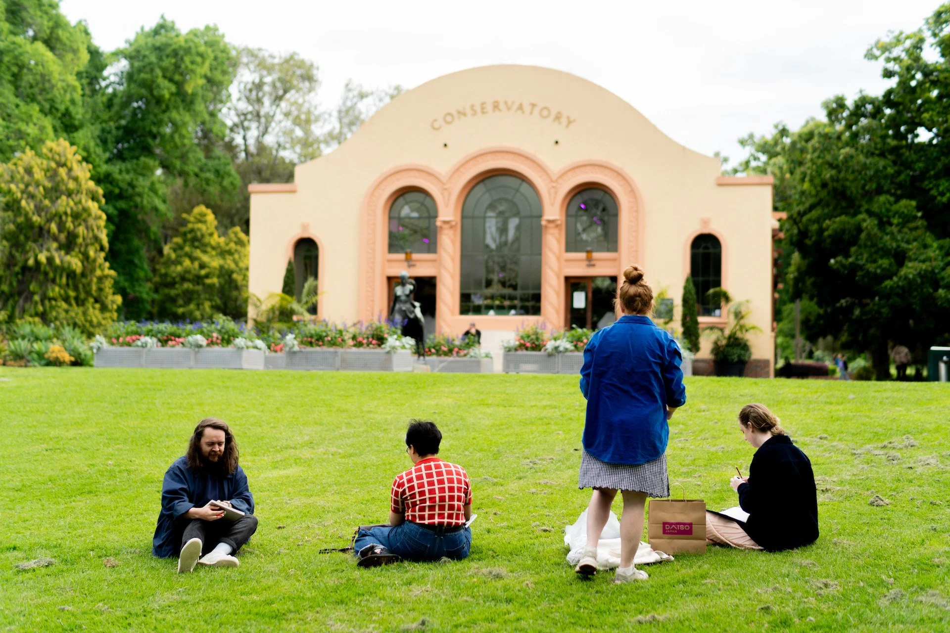 A group of people sketching while sitting on the grass in front of the Conservatory