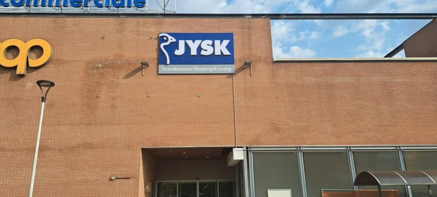 Facciata di un negozio JYSK con un cartello blu e bianco e la scritta "Scandinavian Sleeping & Living".