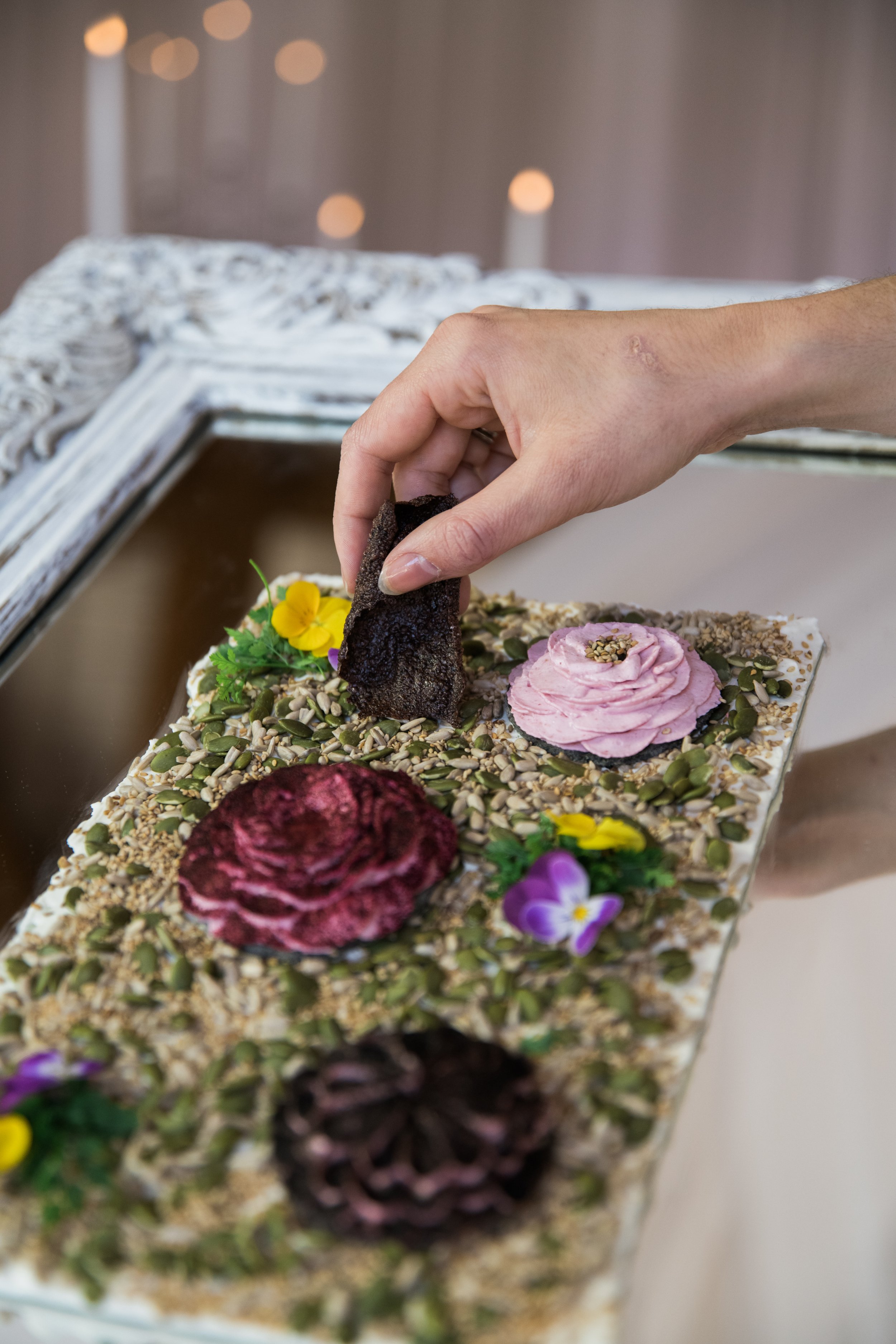 Main déposant un cracker sur un plateau savoureux avec chèvre fouetté betterave et fleurs comestibles dans cadre blanc