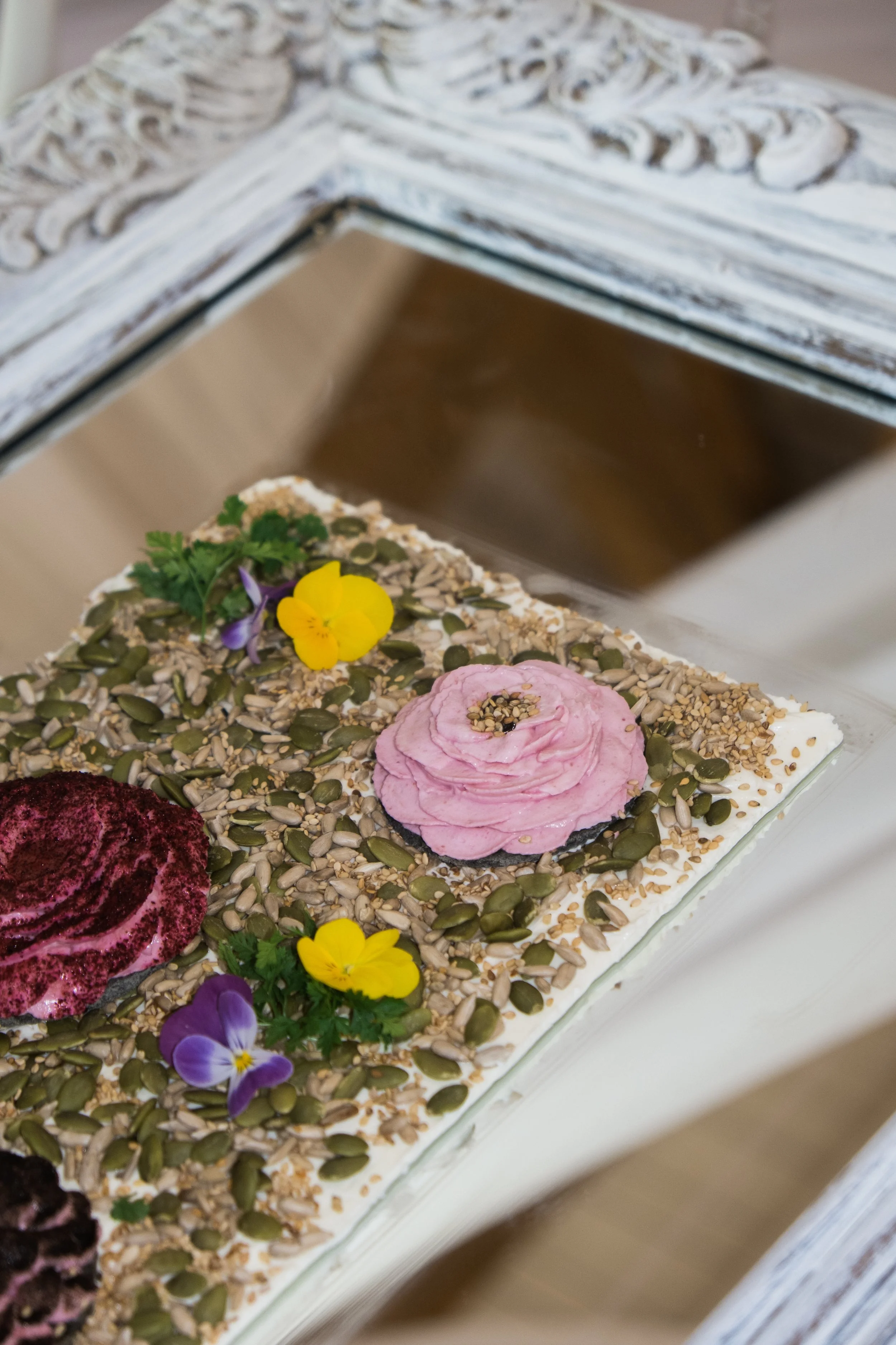 Plateau de houmous blanc aux graines décorés de roses comestibles roses et fleurs violettes