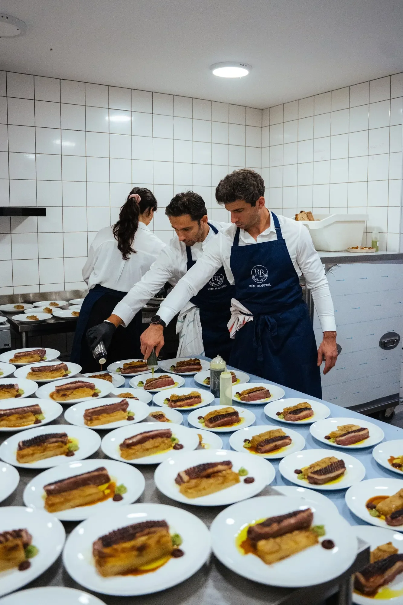 chefs en tablier floqué Rémi Blanpoil dressant simultanément des dizaines d’assiettes identiques