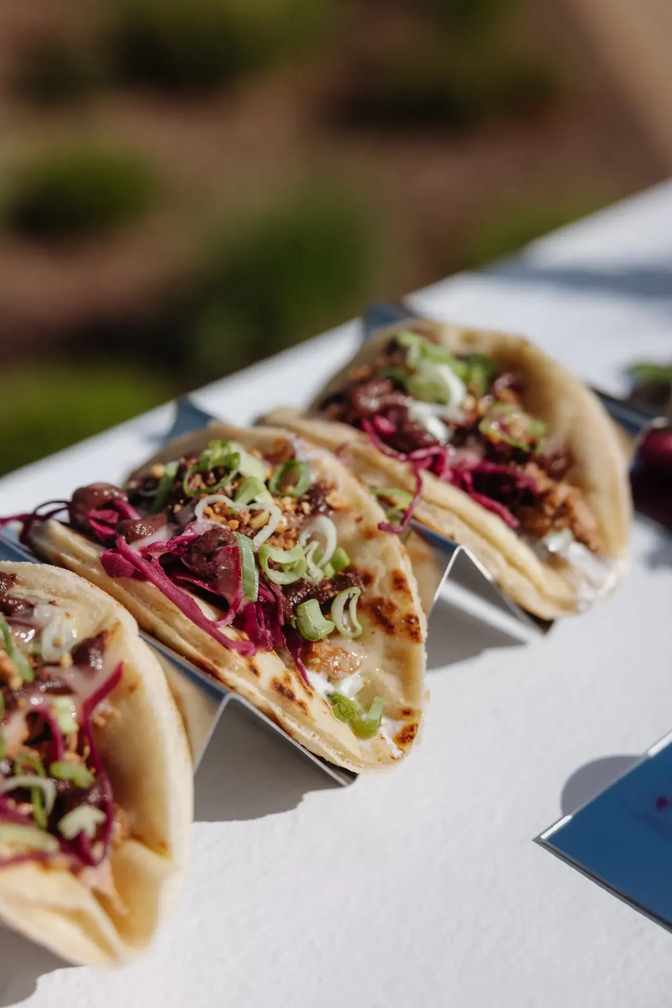 Bouchée façon taco sur galette grillée, viande braisée, chou rouge mariné, cacahuètes concassées et ciboule, servie lors d’une réception traiteur mariage.