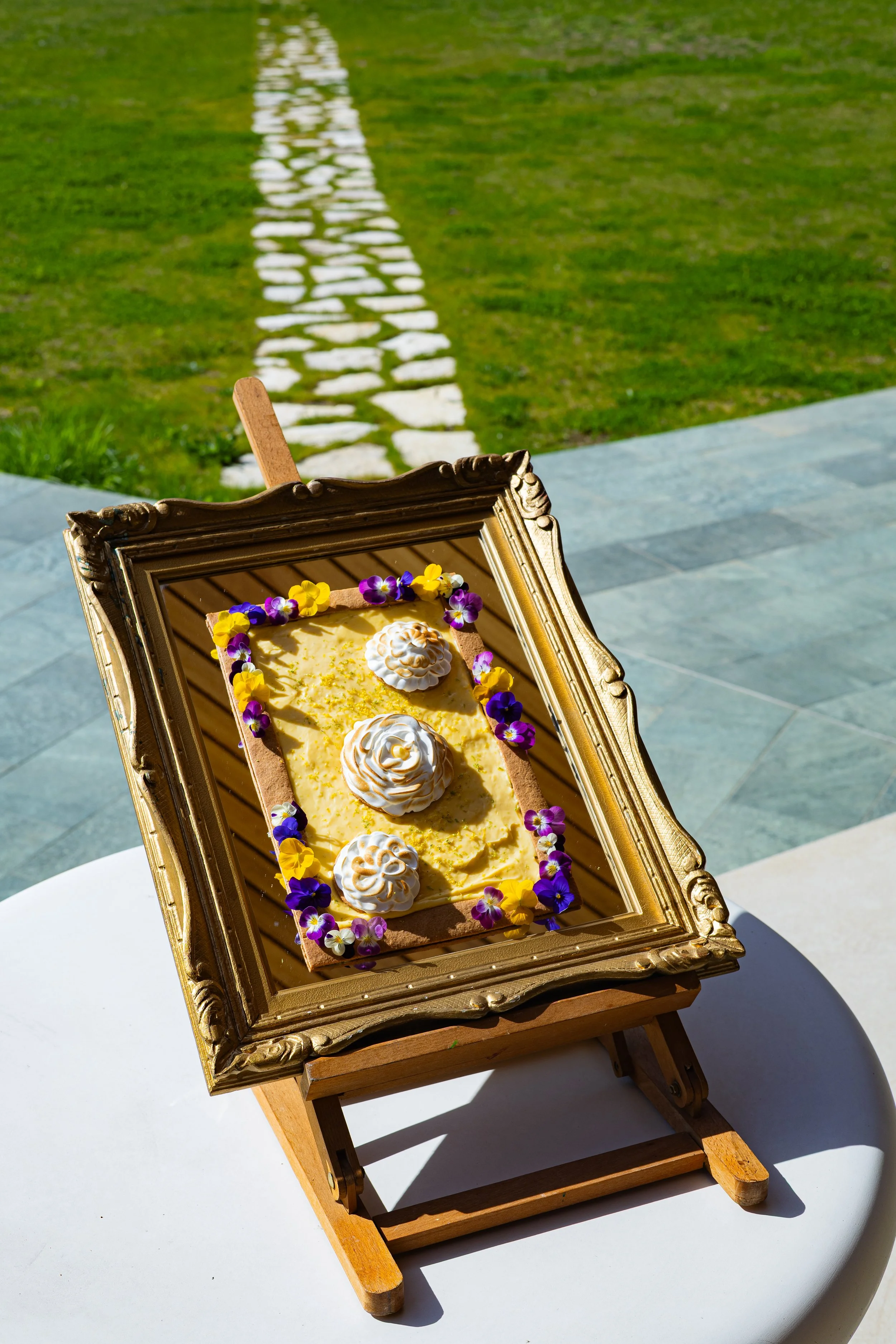 Tarte citron meringuée sur chevalet doré dans un cadre baroque, en extérieur