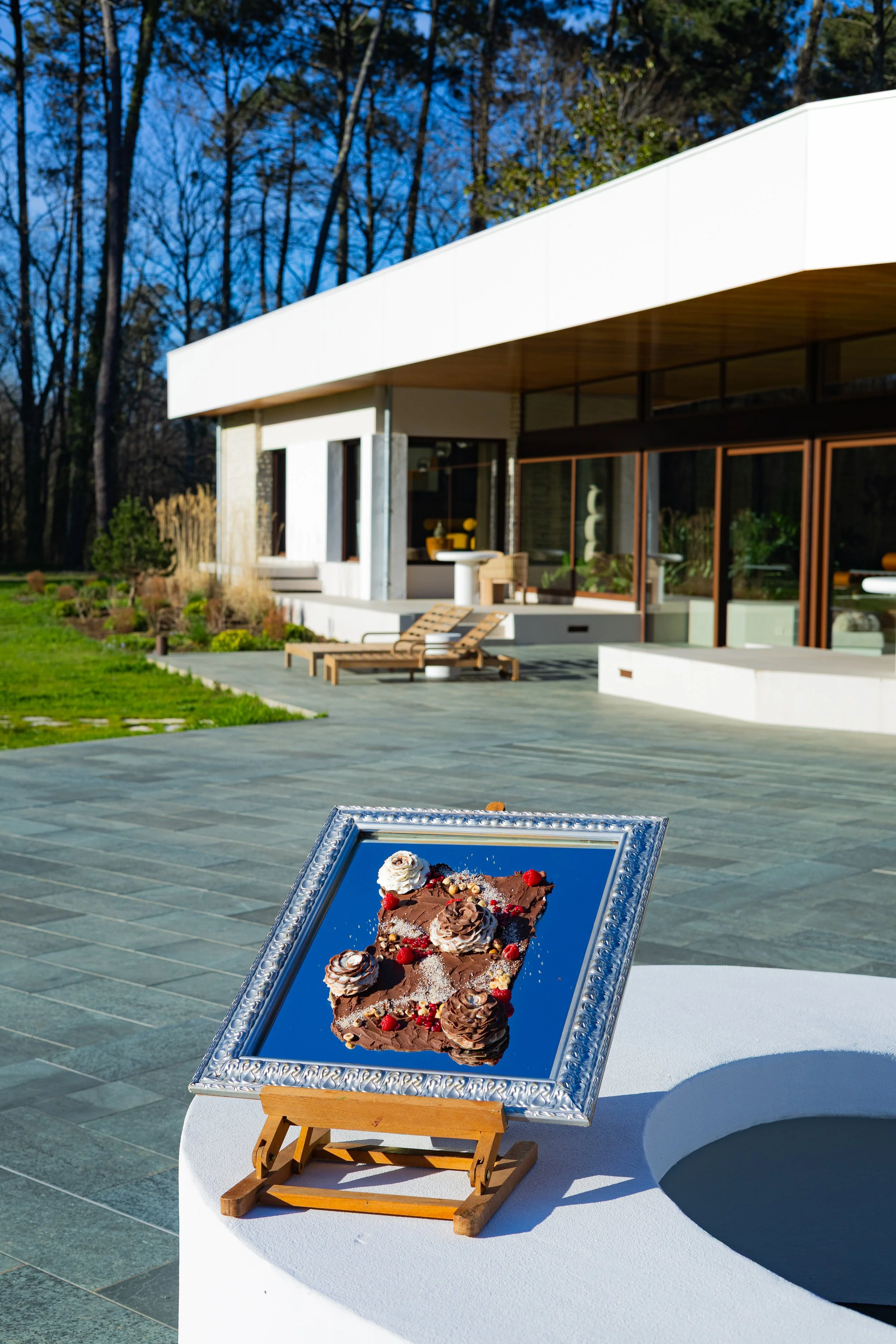 Toile chocolat framboises dans cadre argenté sur chevalet, devant villa moderne