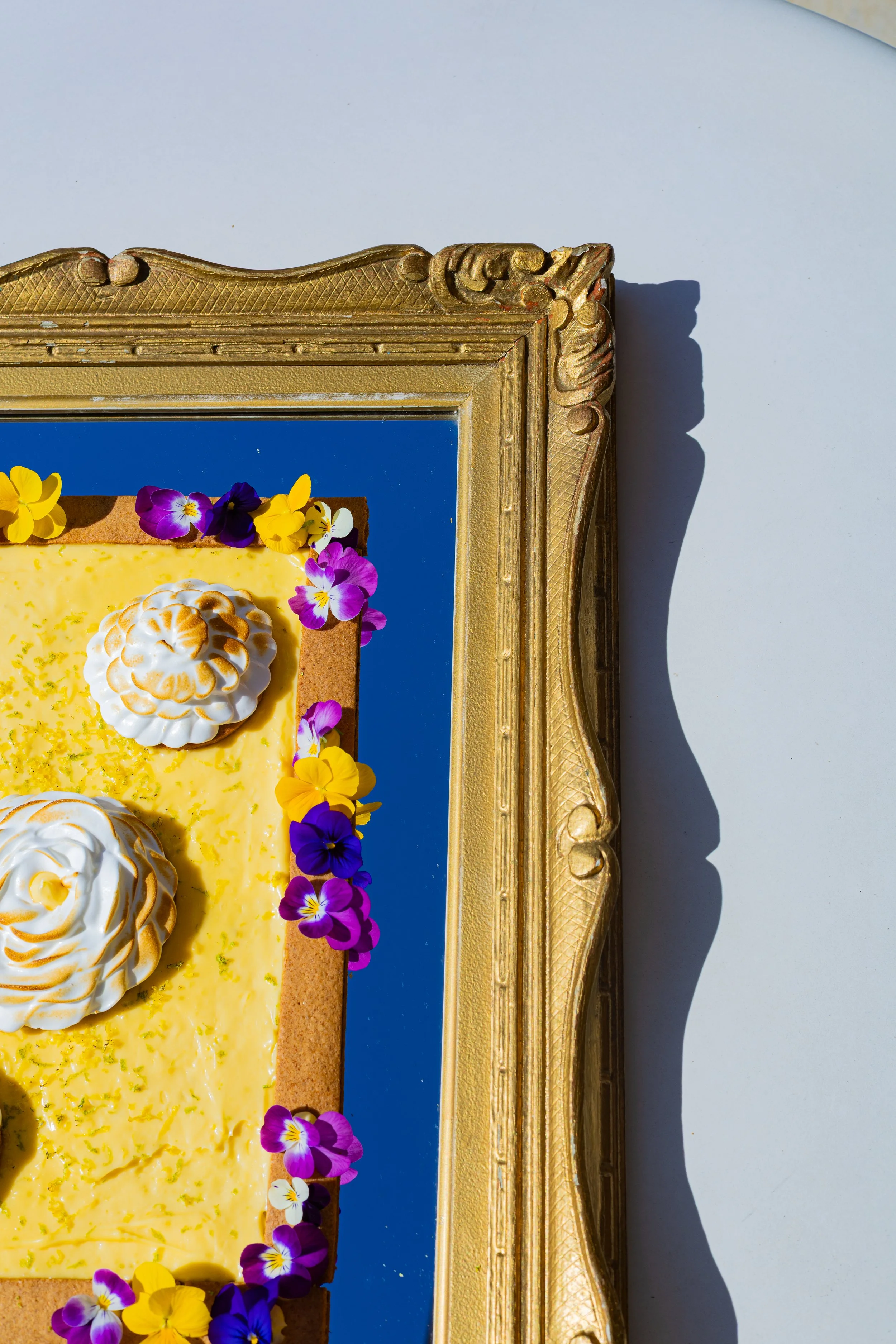 Tarte au citron meringuée présentée dans un cadre baroque doré, décorée de fleurs comestibles violettes et jaunes, par le chef traiteur Rémi Blanpoil à Hossegor, Pays Basque