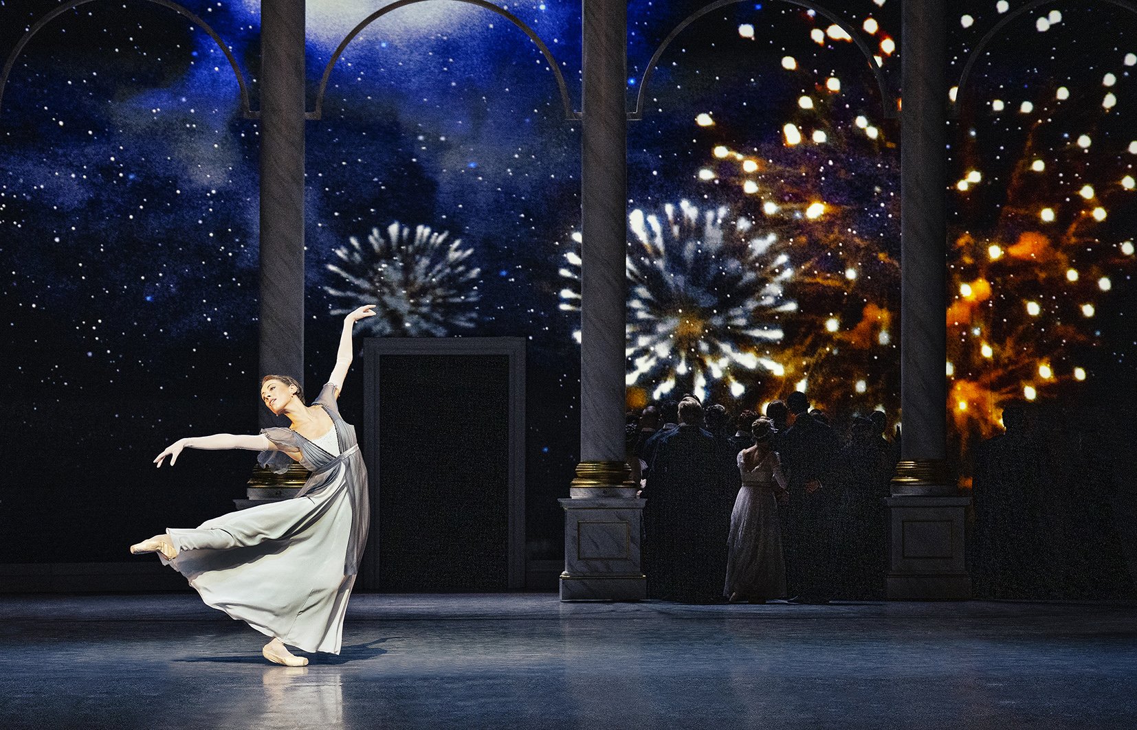 Female ballet dancer on stage in graceful pose with group of New Years guests looking at fireworks projections in the background | Blixen, Det Kongelige Teater.jpg