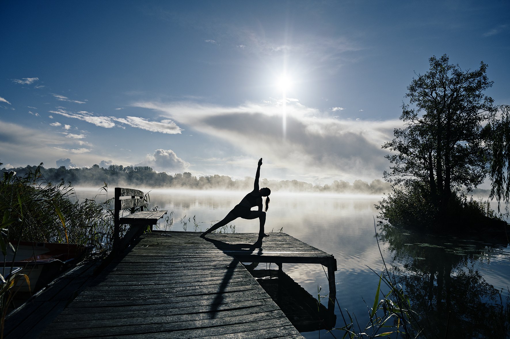 Woman in silhouette in yoga pose on old wooden pier by lake I Backlit and foggy.jpg