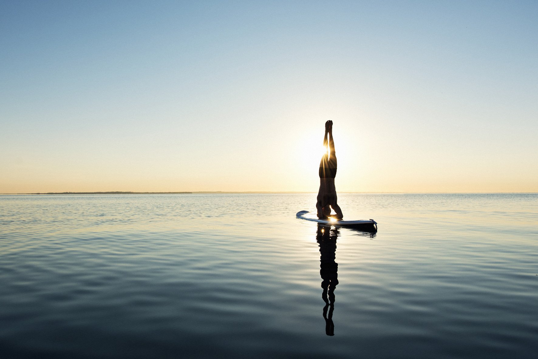 Man doing headstand on a sup board, silhouetted in the sunrise in calm waters.jpg