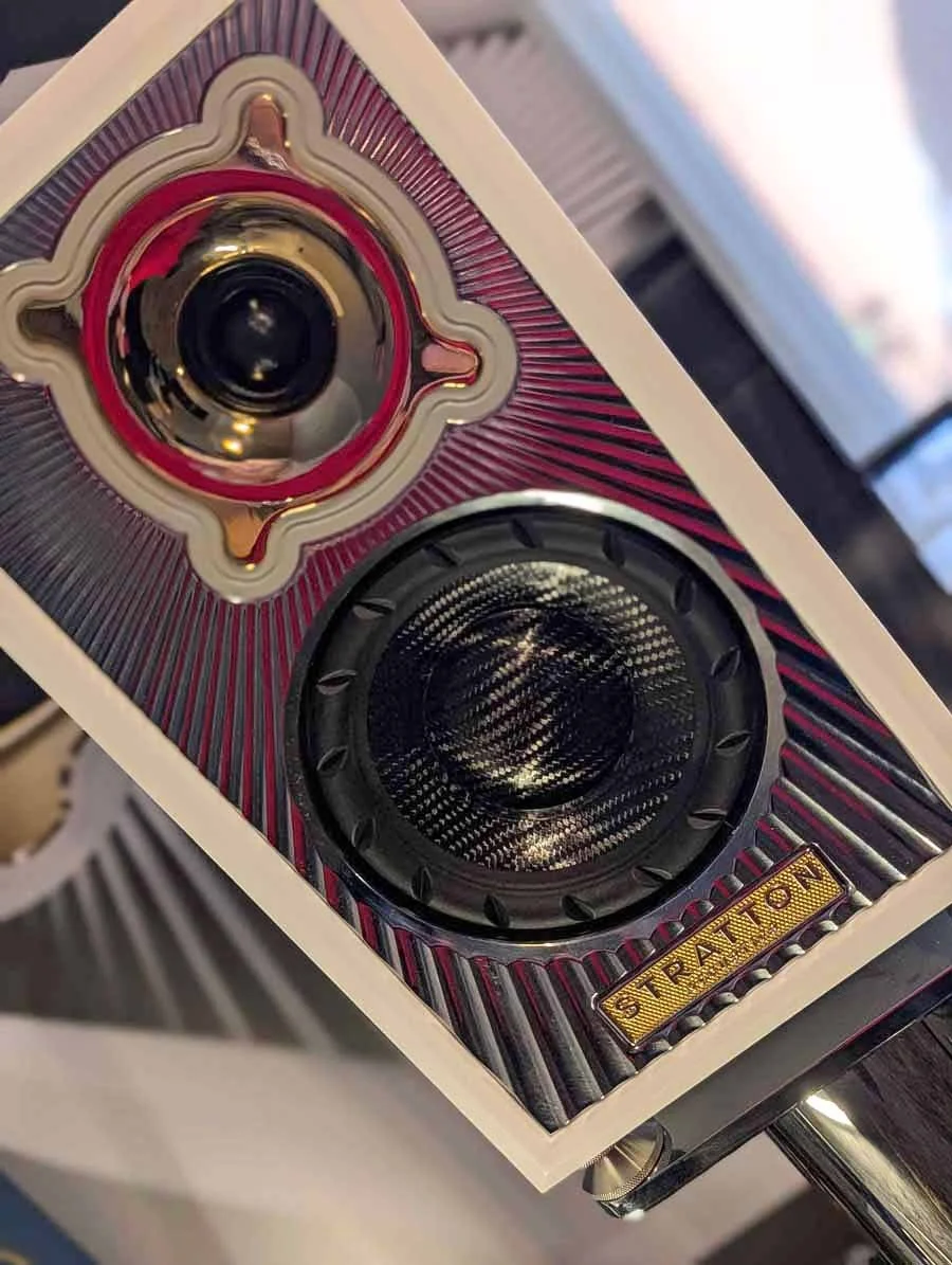 Close-up of the Stratton Acoustics Element 6 high-end speaker with a chrome facia and white casing, showing two large black speaker drivers and a shiny gold horn.