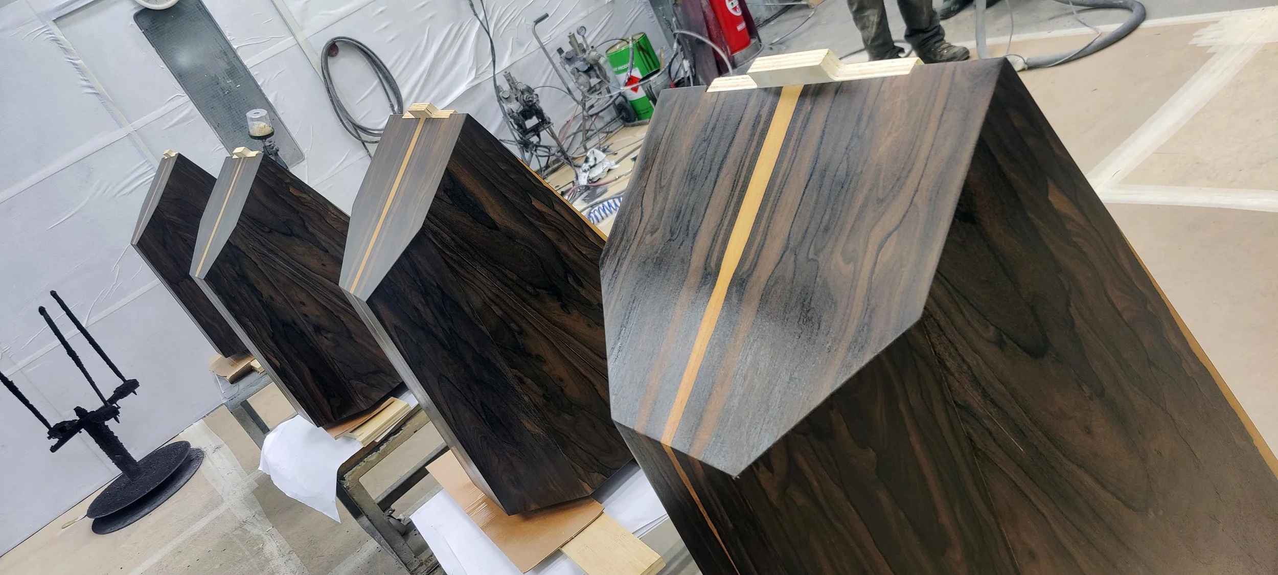 Multiple Stratton Acoustics Element 12 speakers with dark and light wood grains, aligned on workbenches in a workshop setting.