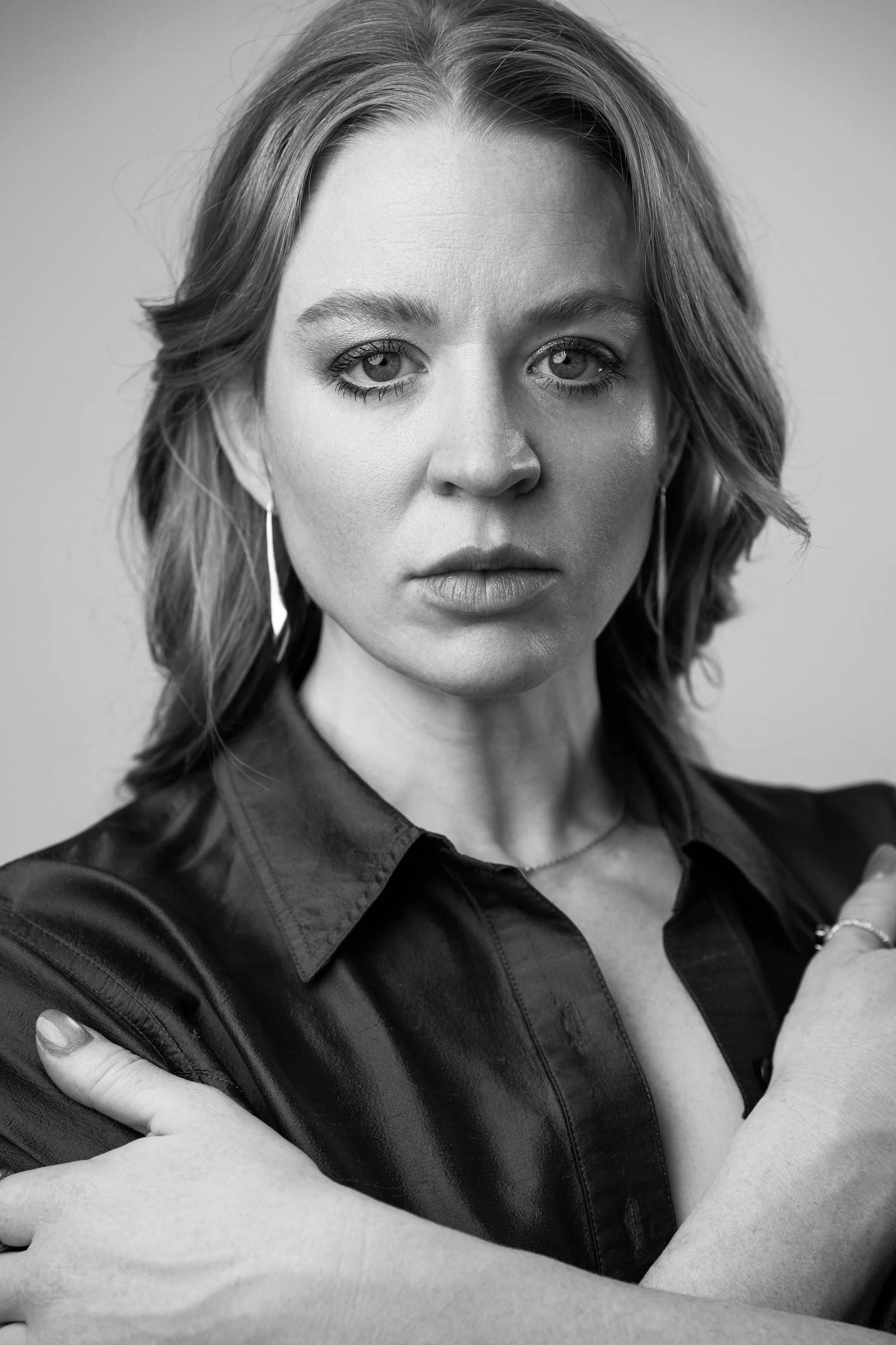Black and white portrait of a woman with shoulder-length hair, wearing a leather jacket, with arms crossed, and looking directly at the camera.