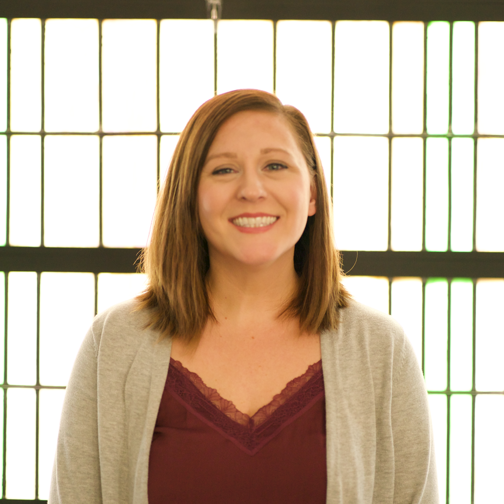 An older man with glasses and a mustache wearing a light blue shirt, standing outdoors with a blurred brick building in the background.