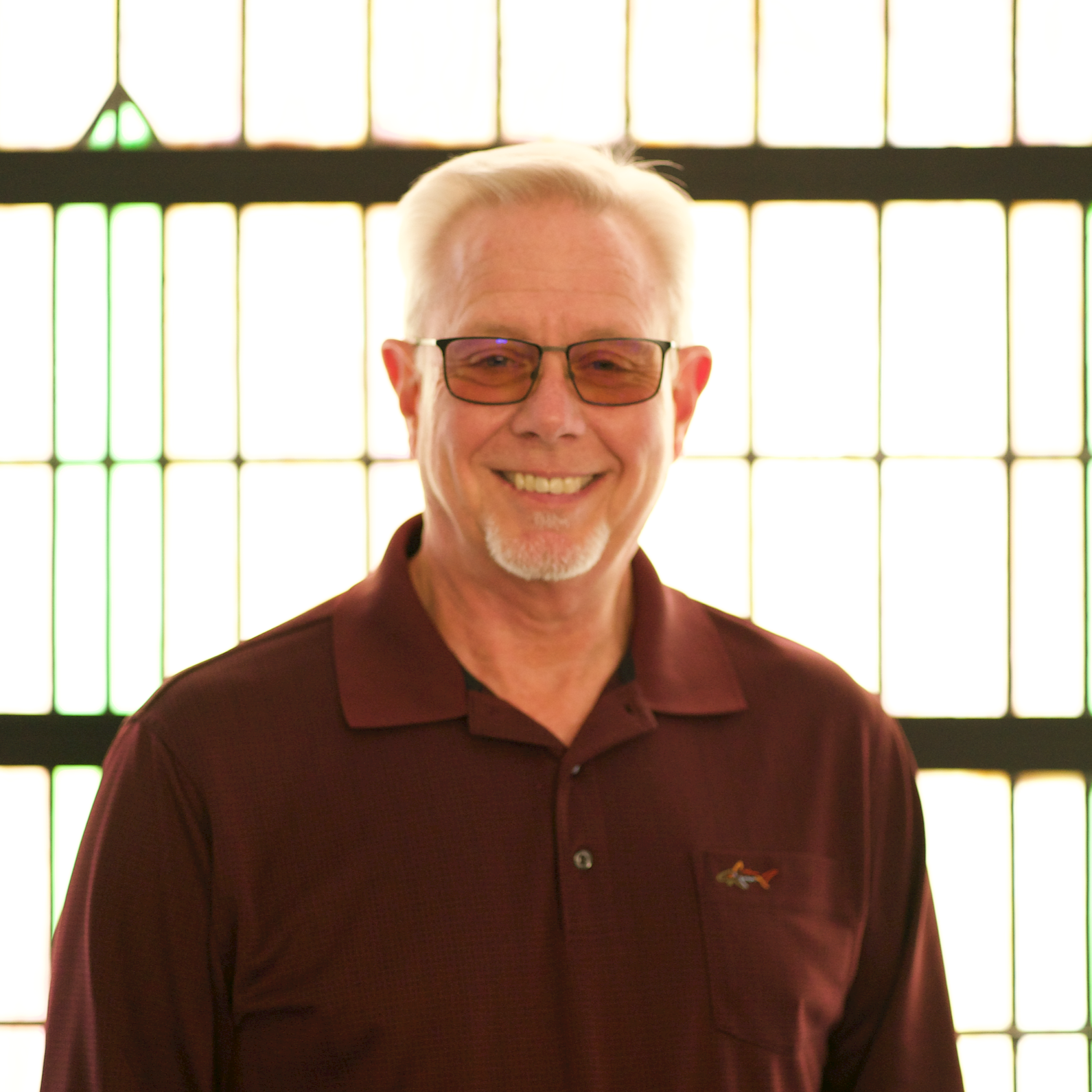 Person wearing glasses and a Callaway zip-up jacket, standing outside near a red brick building with white columns and a green lawn.