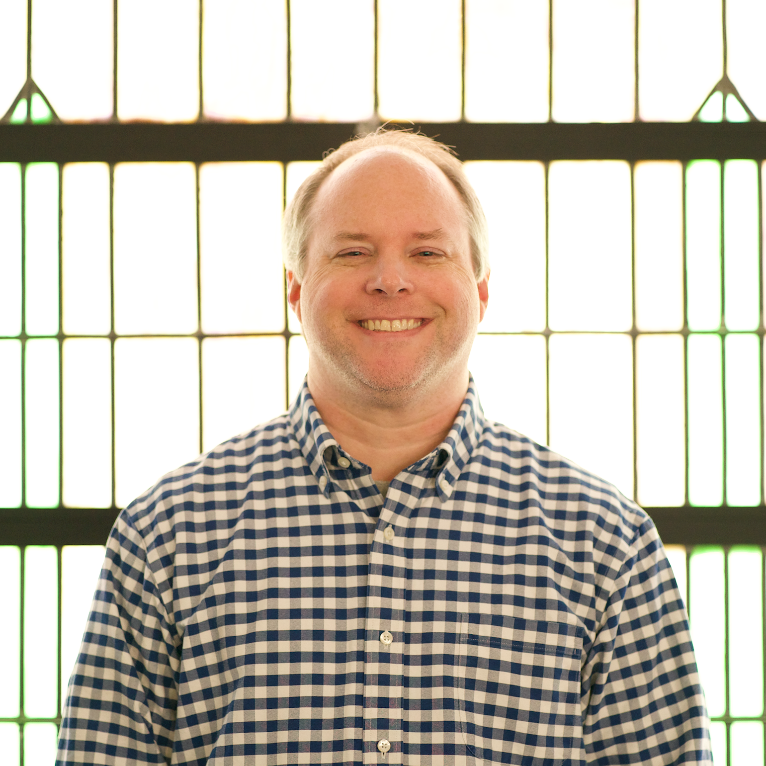 A man with a beard wearing a gray polo shirt stands outside in front of a brick building.
