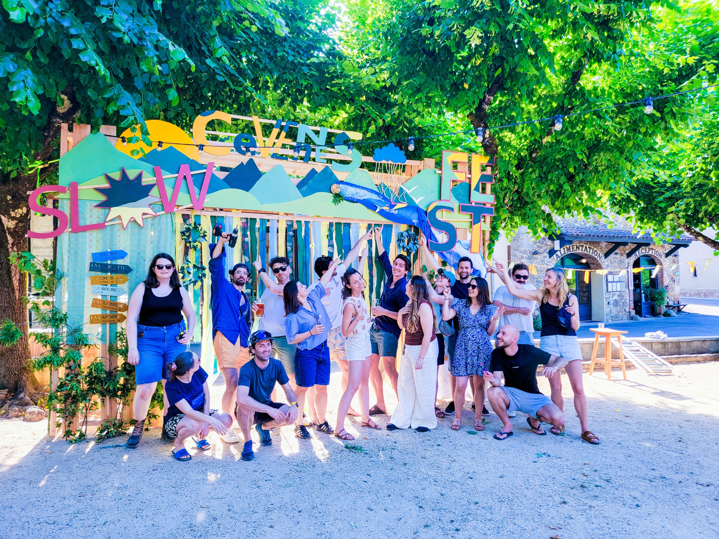 20 participants de l'entreprise Fabriq posent devant une scénographie d'arche en bois réalisée en team building ou séminaire d'entreprise avec Les Briconomes au Slow Village d'Anduze. Atelier de menuiserie créative collaborative.
