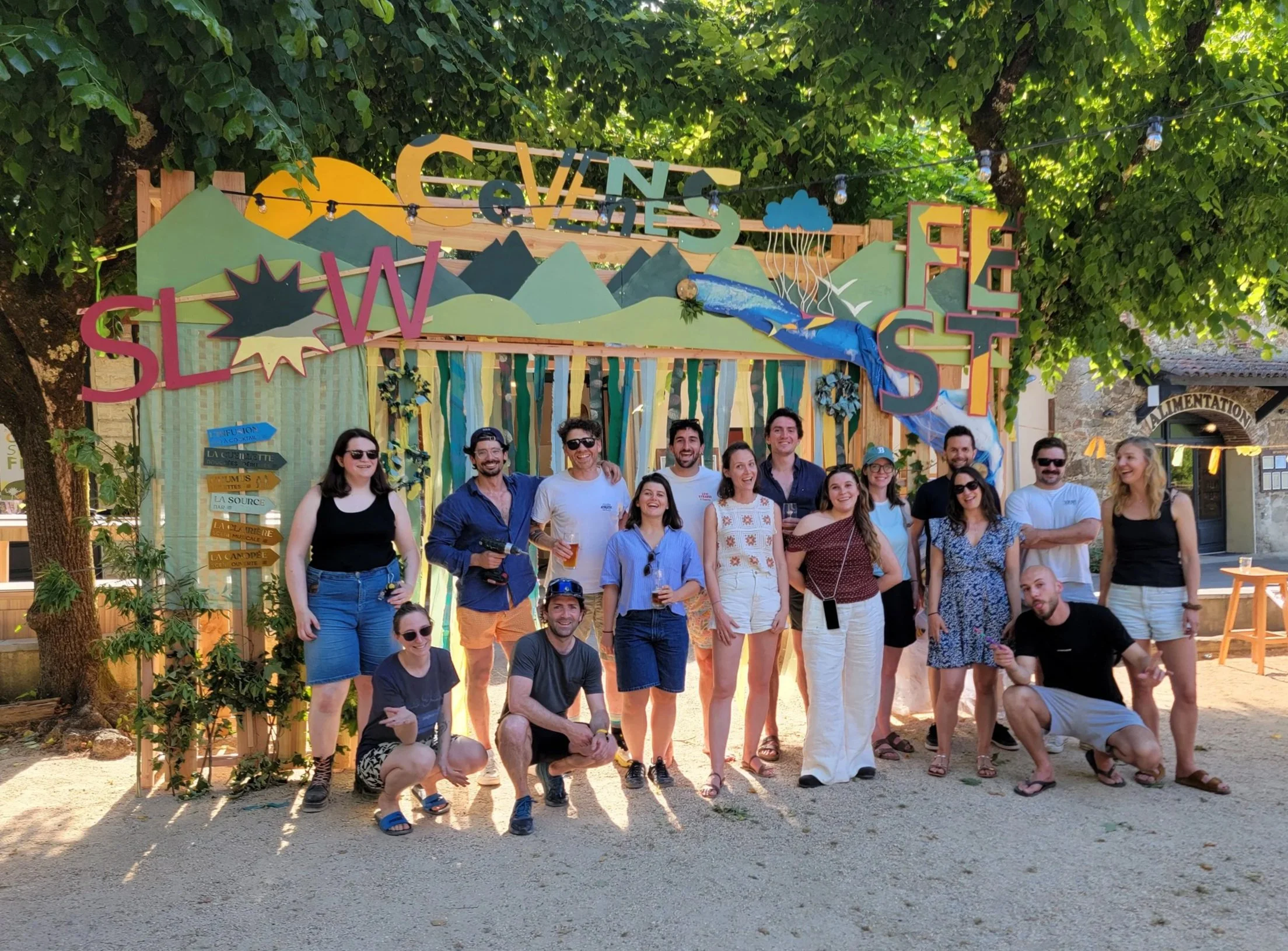 20 participants de l'entreprise Fabriq posent devant une scénographie d'arche en bois réalisée en team building ou séminaire d'entreprise avec Les Briconomes au Slow Village d'Anduze. Atelier de menuiserie créative collaborative.