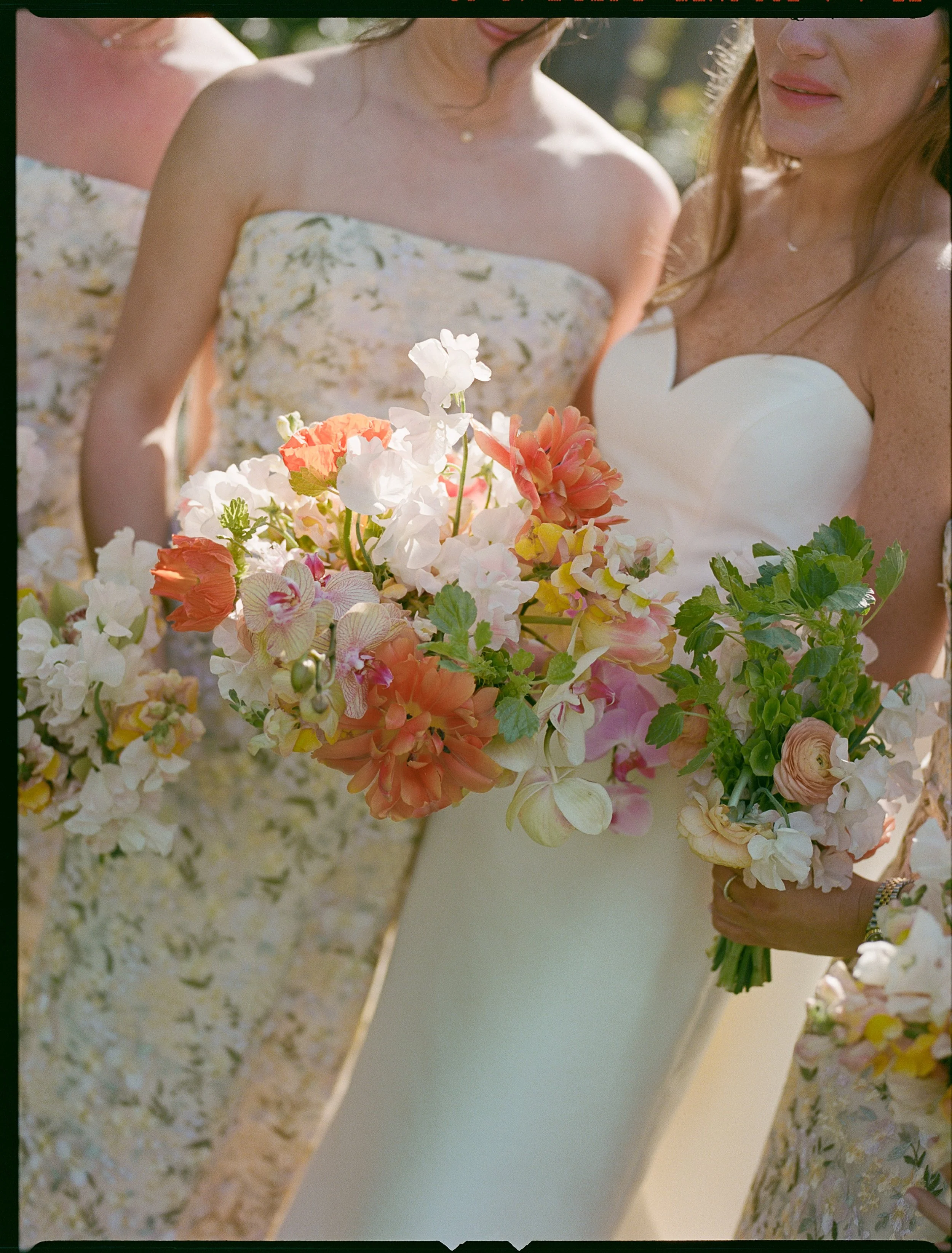 A woman in a white wedding dress holding a large bouquet of pink, white, and peach flowers during a wedding ceremony.
