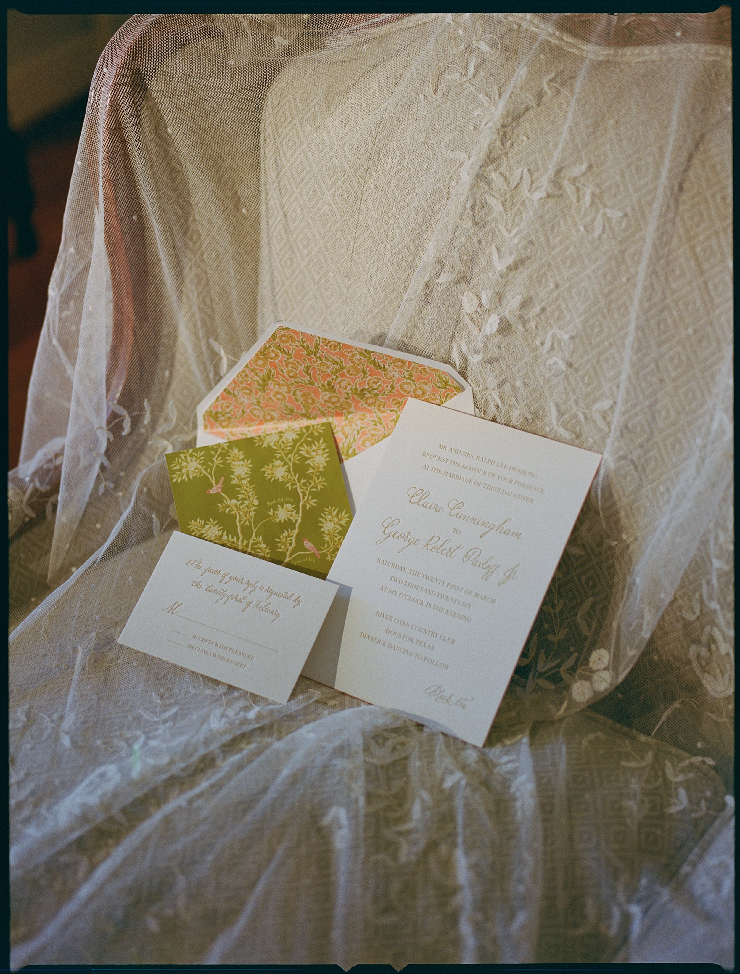 Wedding invitation suite with white invitation, floral patterned envelope, and RSVP card on lace fabric.