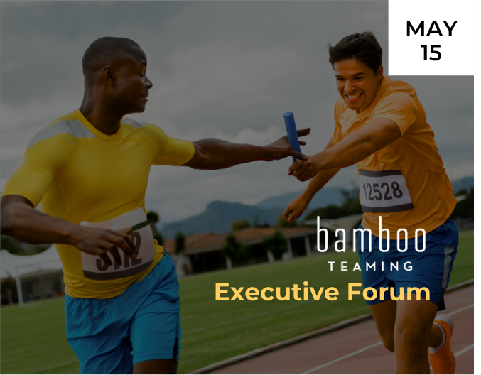 Two relay runners in yellow and blue athletic gear pass a baton on an outdoor track, mid-handoff, with one runner smiling. Mountains and green fields are visible in the background under an overcast sky.