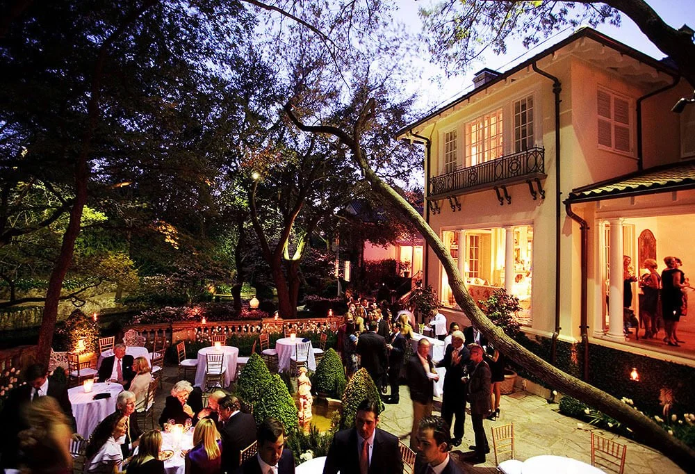 Guests mingling and socializing at an elegant outdoor event, with a large building in the background.