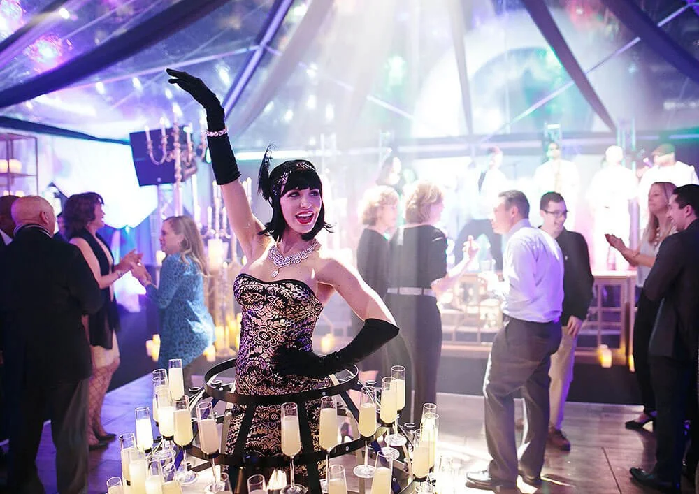 Woman in a glamorous outfit and headpiece dancing at a lively event under colorful lighting.