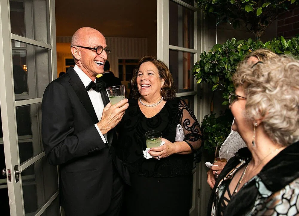 Man and woman dressed in formal attire, smiling and holding drinks at an elegant event.