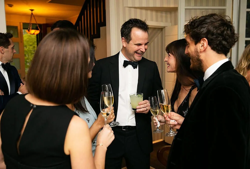 Man in formal attire mingling and toasting with guests at an elegant event.