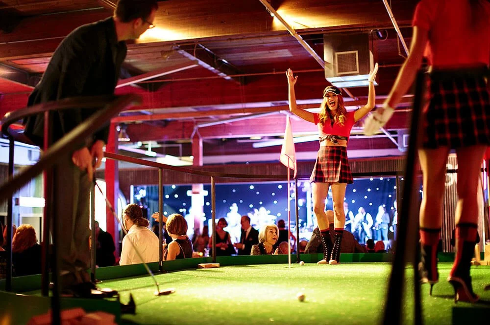 People enjoying a game of mini-golf indoors, with festive lighting and decorations.