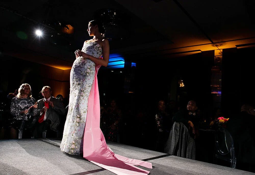 Woman in a stunning gown walking on stage, illuminated by spotlights.