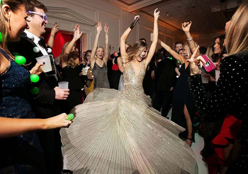 Bride in a glamorous wedding dress celebrating on the dance floor with guests cheering.