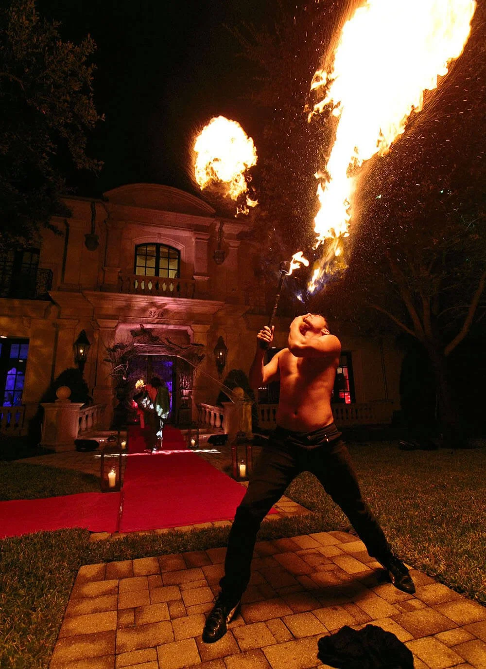 Fire performer entertaining guests at an outdoor event, spinning flaming props in a dramatic display.