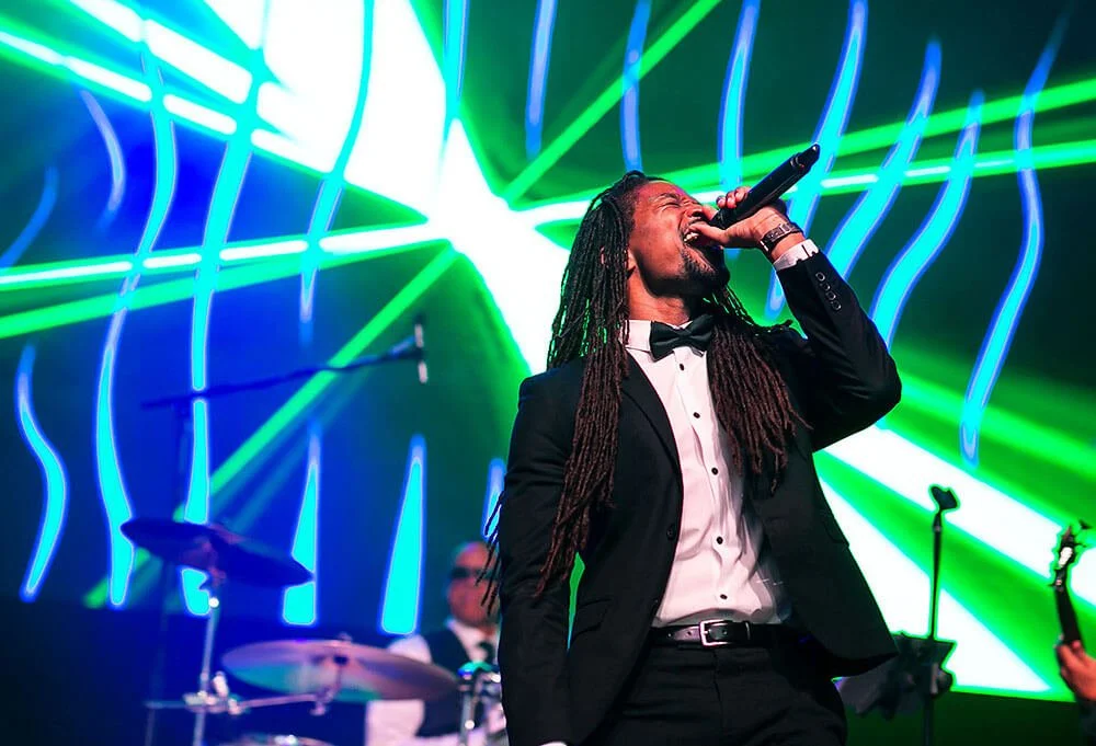 Performer singing passionately on stage with vibrant, colorful lighting in the background.