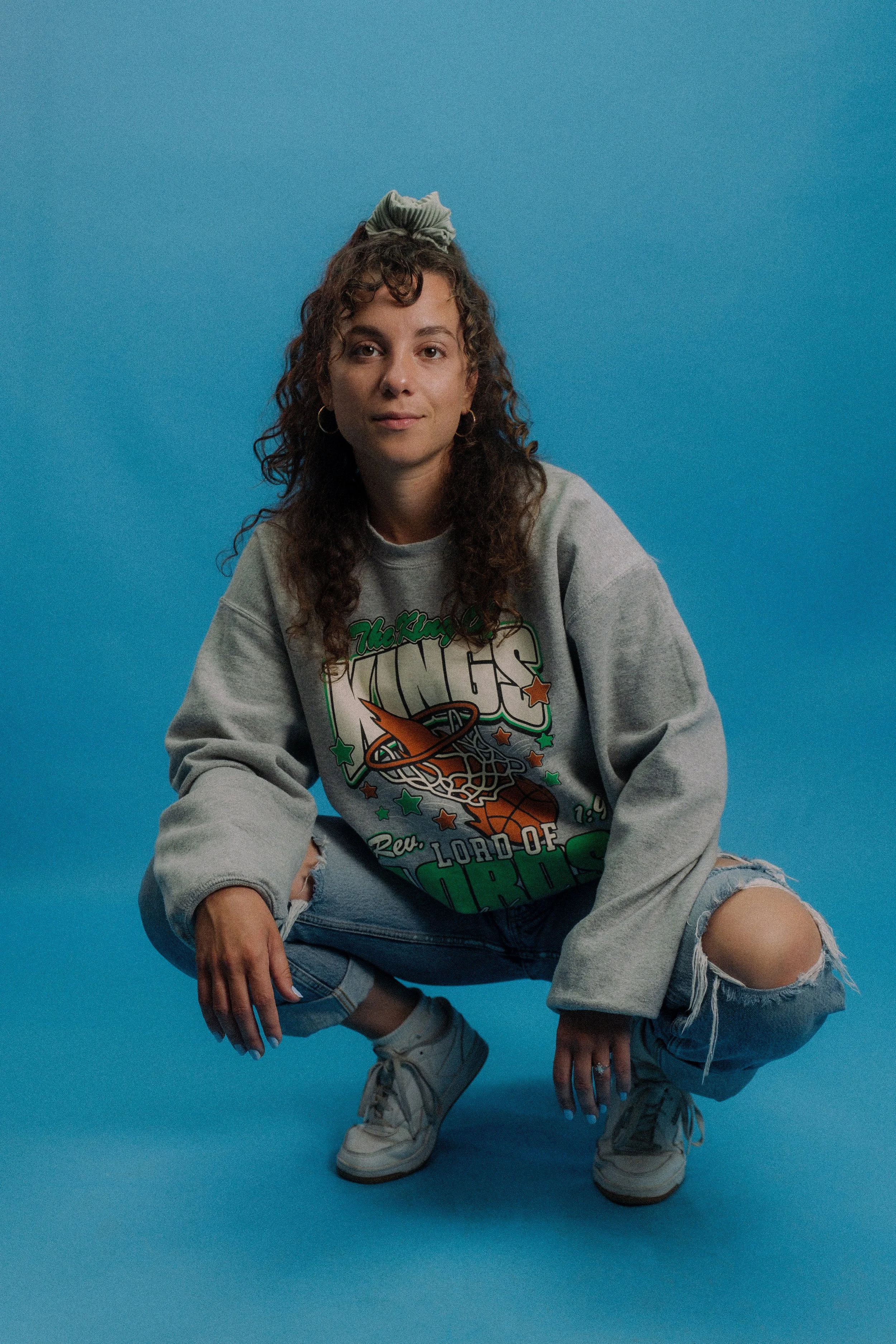 Woman modeling vintage crewneck shirt against blue backdrop.