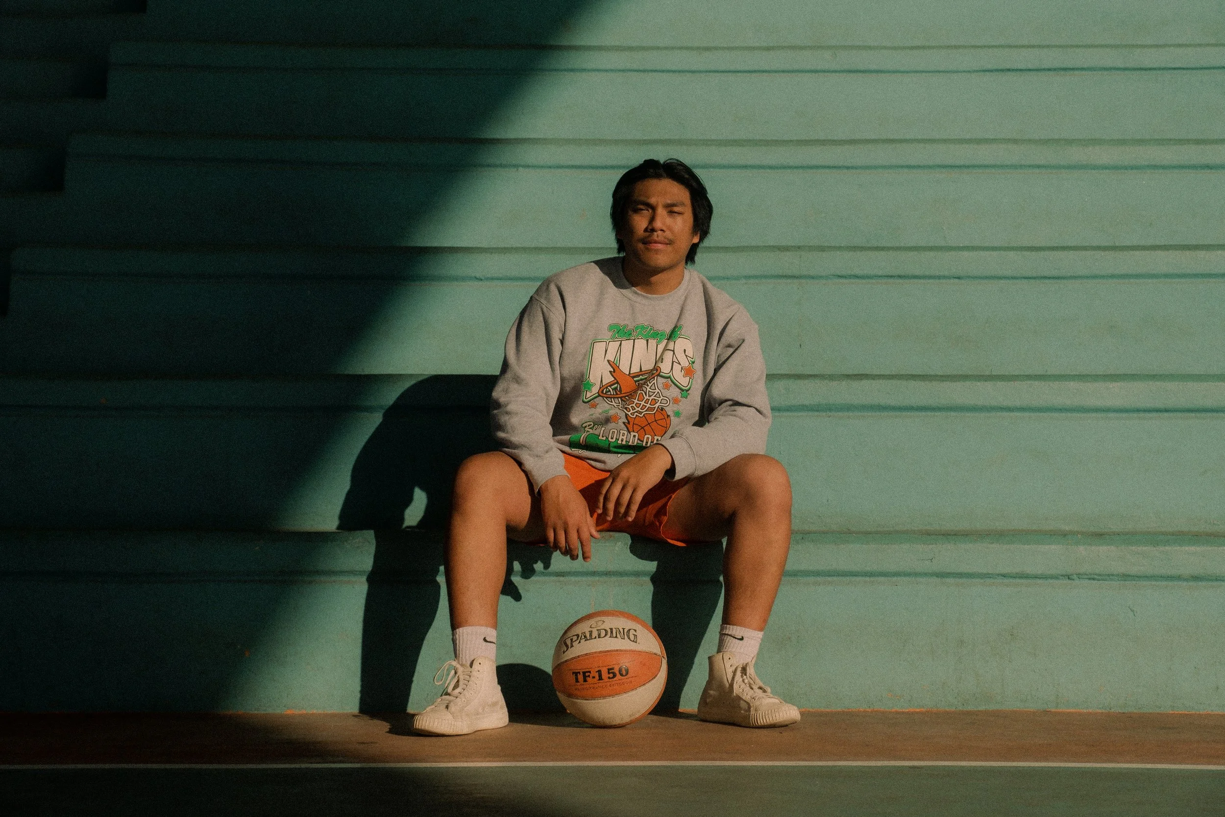 Man sitting on bleachers with basketball between his feet.