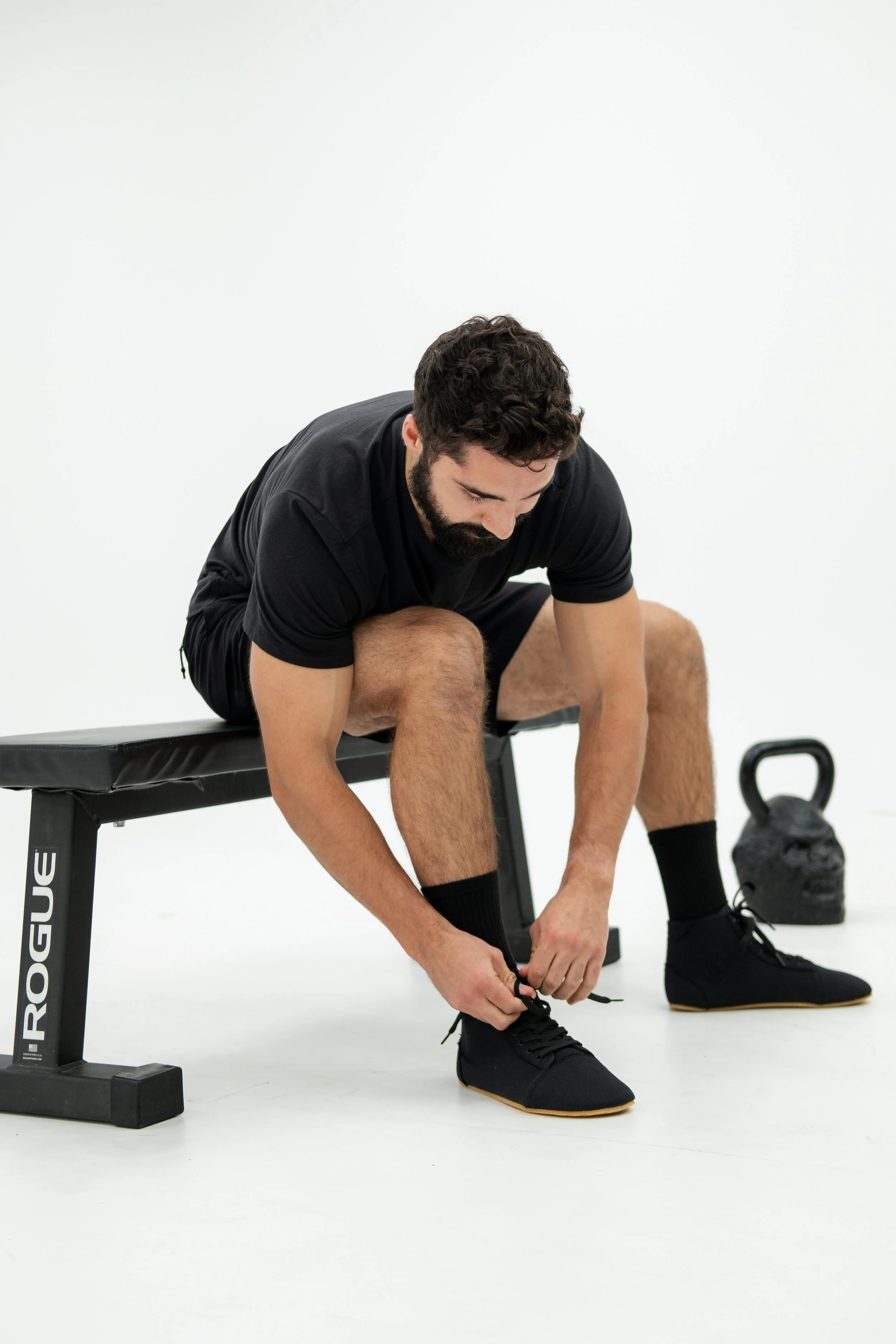 Man on bench tying his shoe with kettlebell in the background.