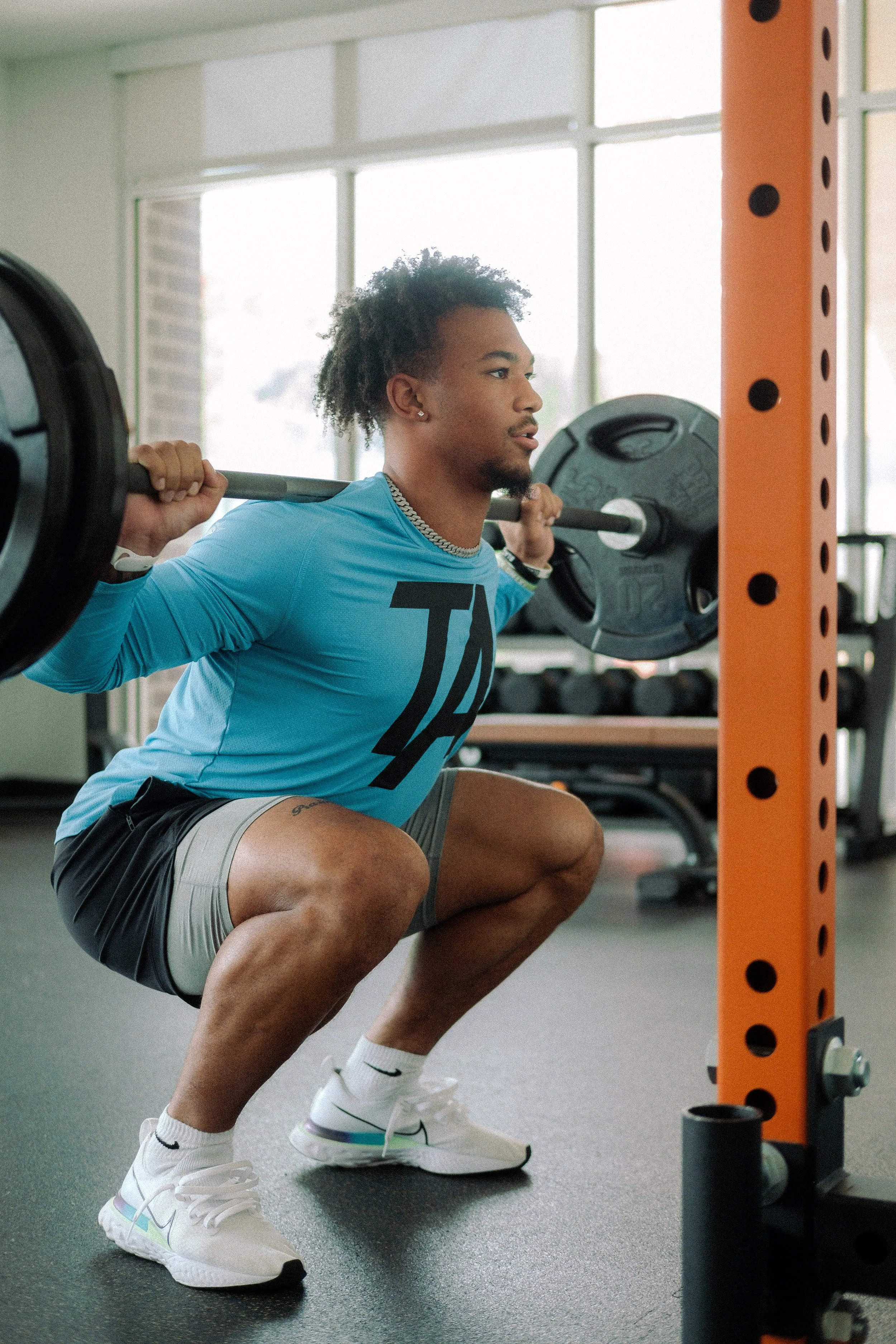 Black man in blue shirt doing barbell squats.